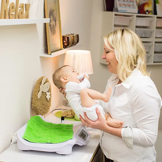 Hebamme hebt ein Baby von der Babywaage